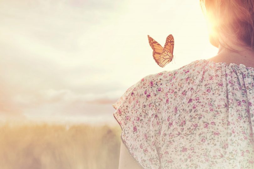 woman in a field with a butterfly on her shoulder